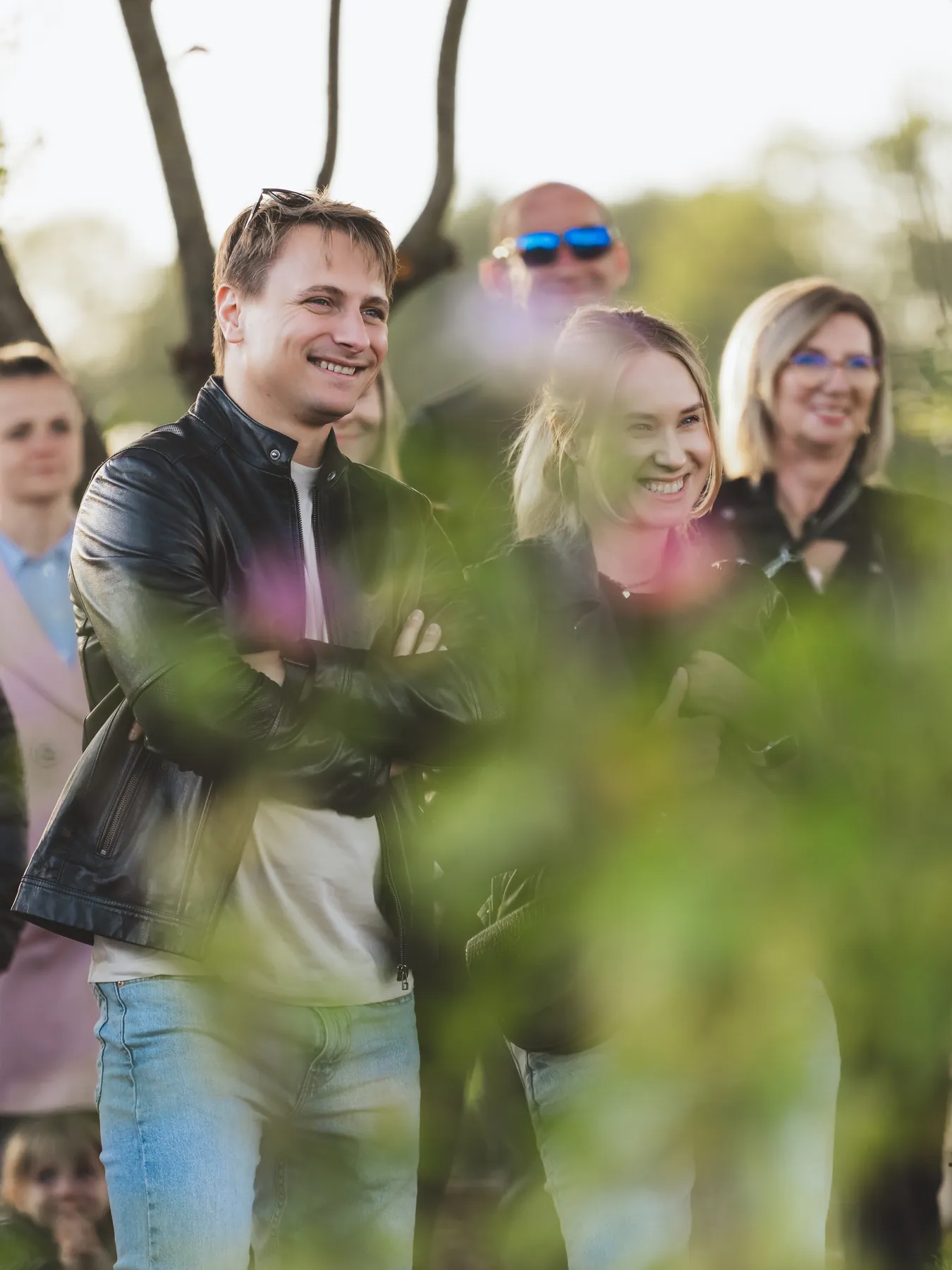 Uśmiechnięci goście eventu w&nbsp;plenerze, zieleń w&nbsp;pierwszym planie