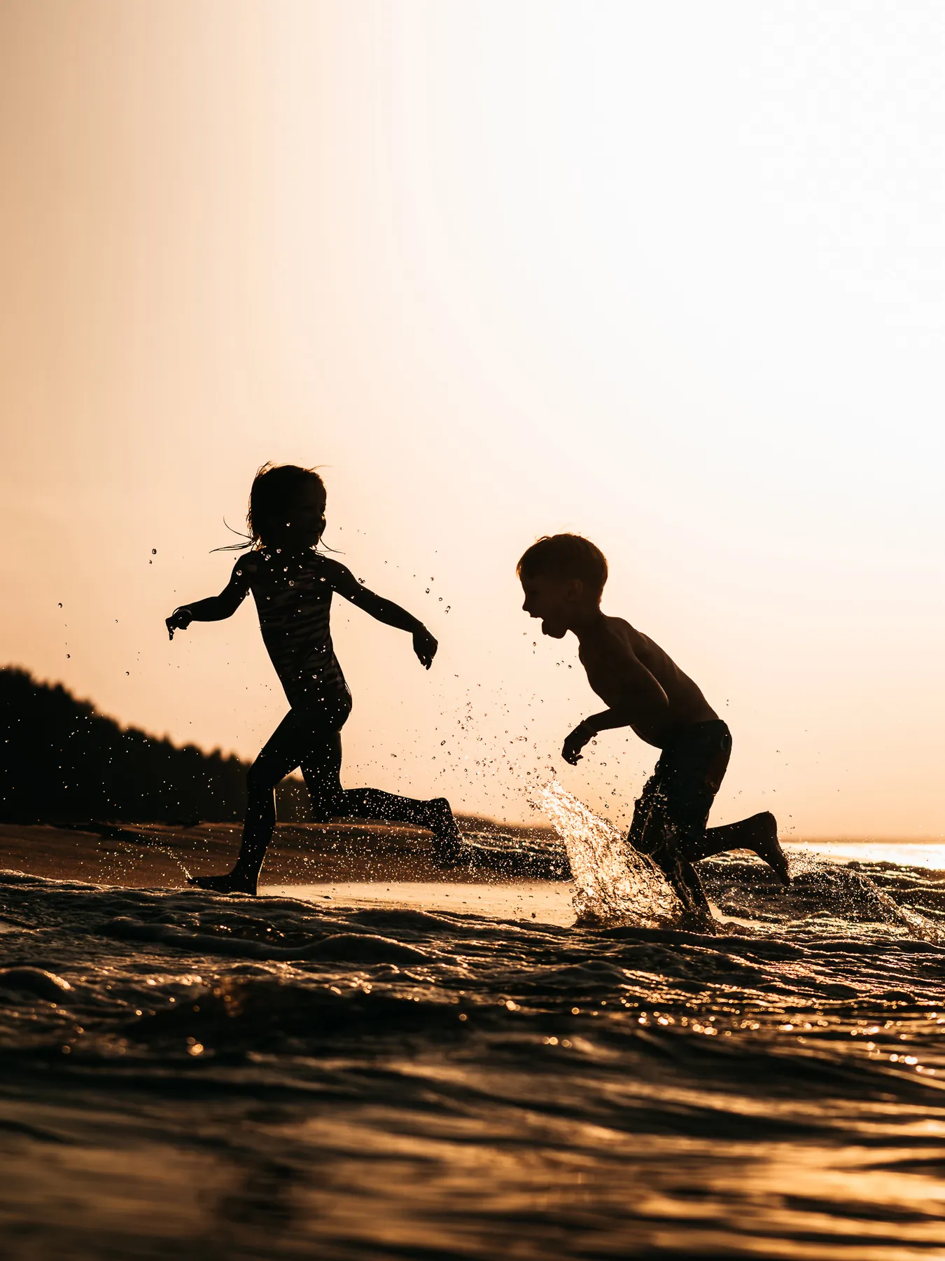 Dzieci biegają po wodzie na plaży o&nbsp;zachodzie słońca